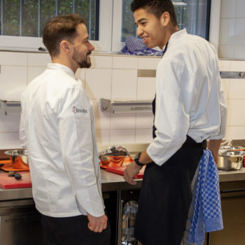 Koch-Azubi Tomas Njie (rechts) und Berufsschullehrer Markus Wolf im Praxisunterricht. Foto: VKD